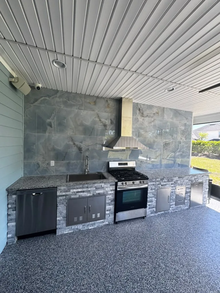 Completed GS One outdoor kitchen with a stone backsplash, stainless steel grill and range hood